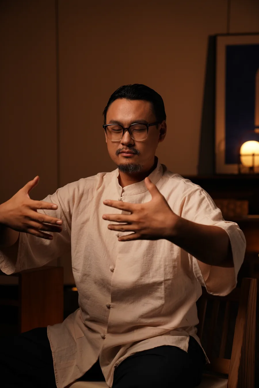 Master Lao seated, hands closing towards the chest, eyes lowered.