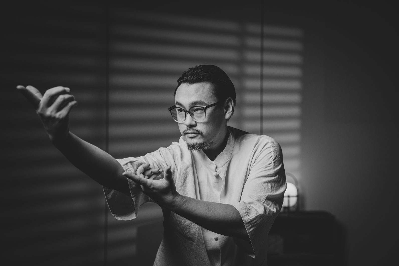 Master Lao practising taiji in slatted window light, one arm extended.